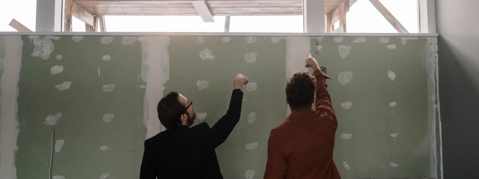 Zwei Monteure verspachteln die Schraubenköpfe einer frisch beplankten Trockenbauwand.