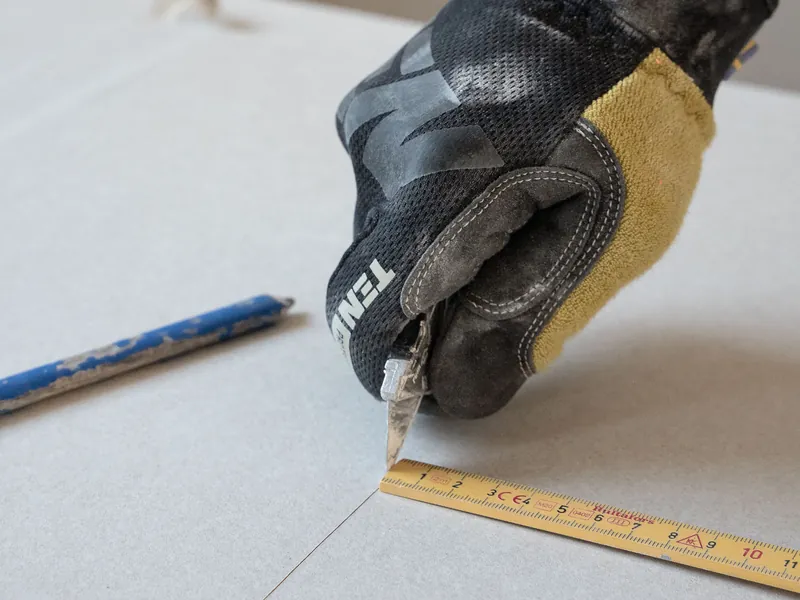 Nahaufnahme: Zuschnitt einer Gipskartonplatte mit dem Cuttermesser entlang des Zollstocks.